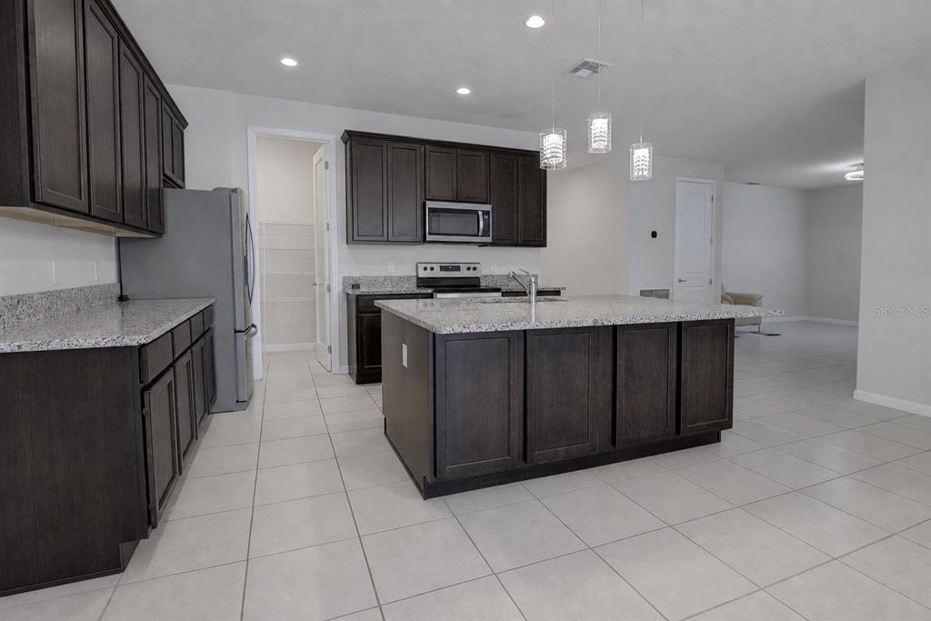 A kitchen features dark wood cabinets, granite countertops, a central island, and light tile flooring — 3552 STONEBRIAR LANE, SANFORD, FL