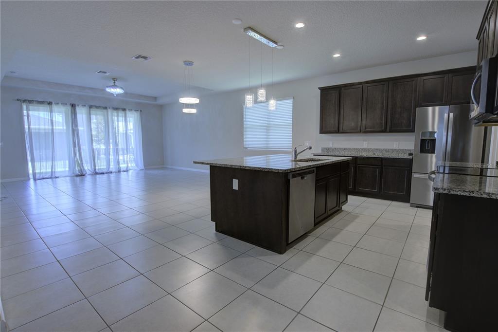 A kitchen with dark cabinets and a granite island opens into a large tiled living area — 3552 STONEBRIAR LANE, SANFORD, FL