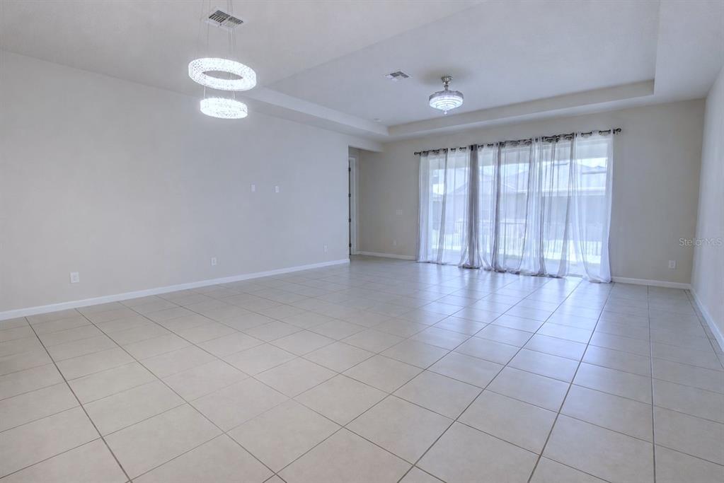 An empty living room features light tile flooring, a tray ceiling, and sliding glass doors — 3552 STONEBRIAR LANE, SANFORD, FL