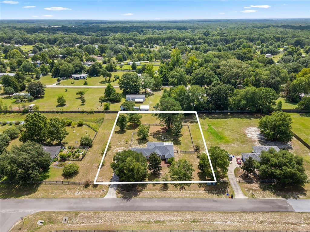 An aerial view shows a house with a fenced yard surrounded by trees and fields — 9445 SW 96TH TERRACE, GAINESVILLE, FL