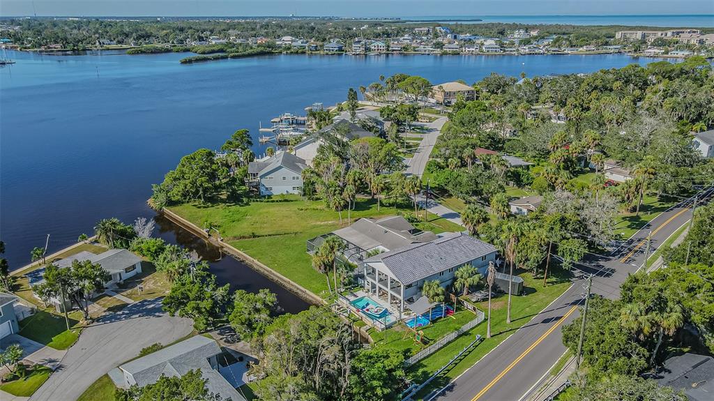 An aerial view shows a waterfront house with a pool, lawn, and surrounding neighborhood — 5254 MILLER BAYOU DRIVE, PORT RICHEY, FL
