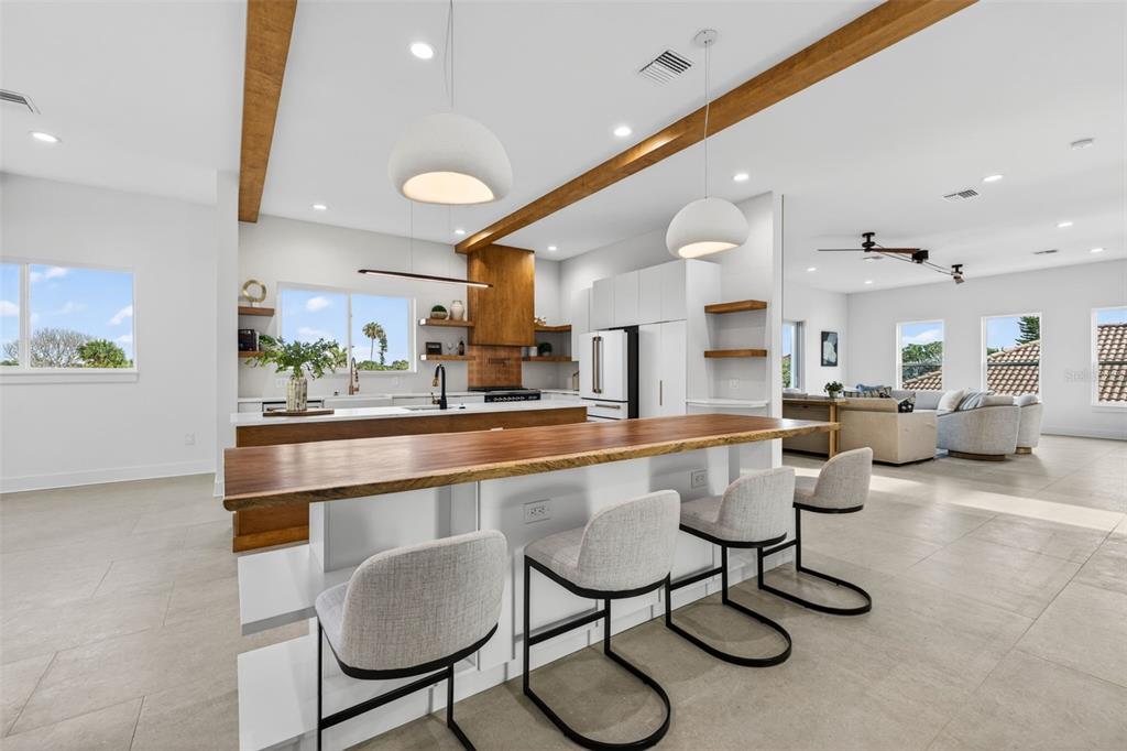 A modern kitchen features a live-edge wood island, white cabinetry, and exposed ceiling beams — 3221 GULF BOULEVARD, BELLEAIR BEACH, FL