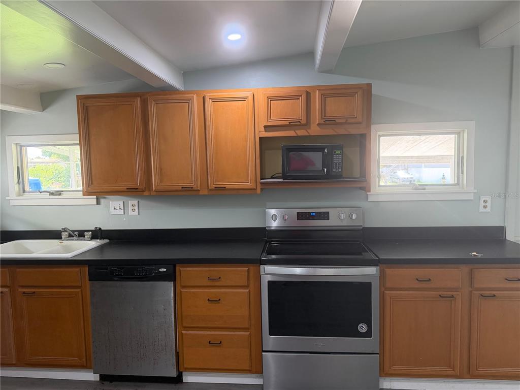 A kitchen features wood cabinets, black countertops, stainless steel appliances, and two windows — 6967 POMPEI ROAD, ORLANDO, FL