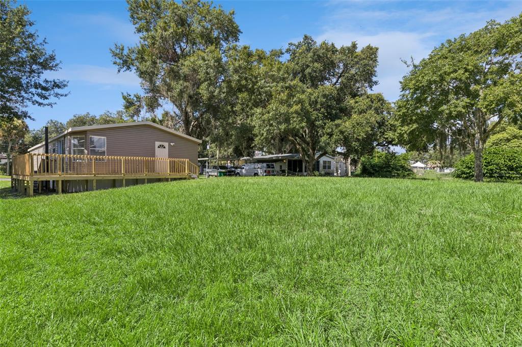A large grassy yard leads to a mobile home with a wooden deck and trees — 5038 CAMBRIDGE DRIVE, MIMS, FL