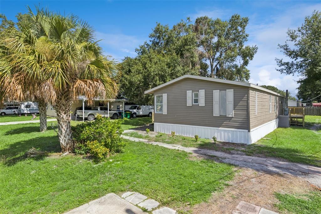 A tan mobile home with white trim sits on a grassy lot with a palm tree — 5038 CAMBRIDGE DRIVE, MIMS, FL