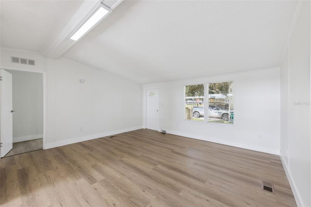 A bright, empty living room features white walls, light wood-look flooring, and a large window — 5038 CAMBRIDGE DRIVE, MIMS, FL