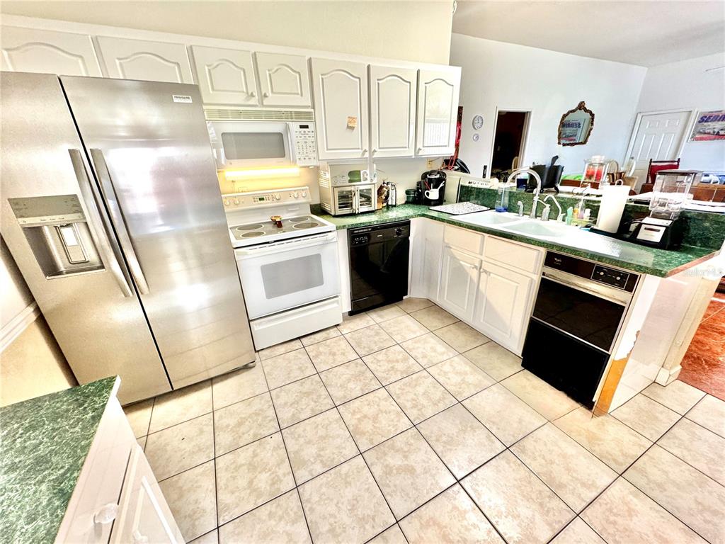 A kitchen features white cabinets, stainless steel appliances, green countertops, and light-colored tile flooring — 2605 BAYVIEW STREET, SEBRING, FL