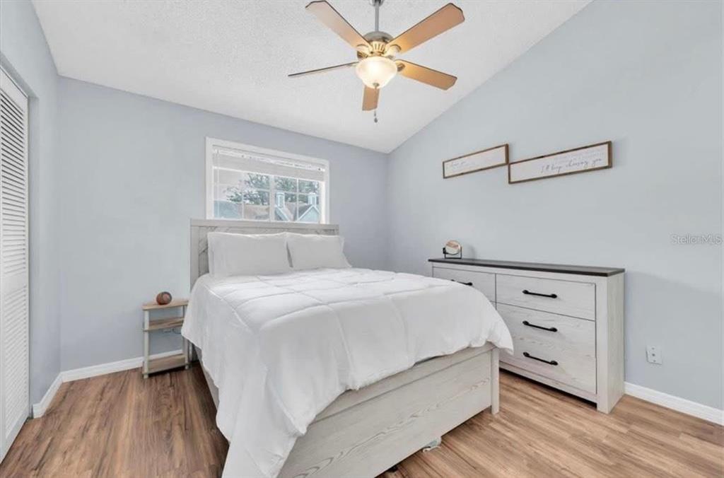 A bedroom features light wood-look flooring, a white bed frame, a dresser, and a ceiling fan — 11338 STRATTON PARK DRIVE, TEMPLE TERRACE, FL