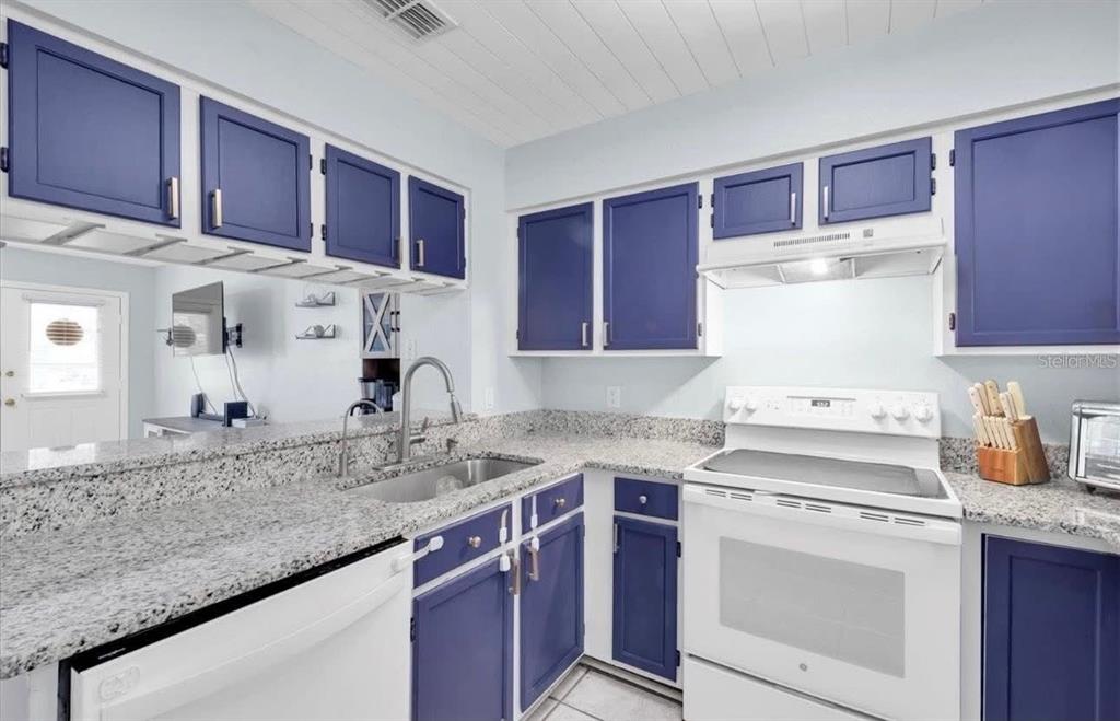 A kitchen features blue cabinets, granite countertops, and white appliances against a light-colored wall — 11338 STRATTON PARK DRIVE, TEMPLE TERRACE, FL