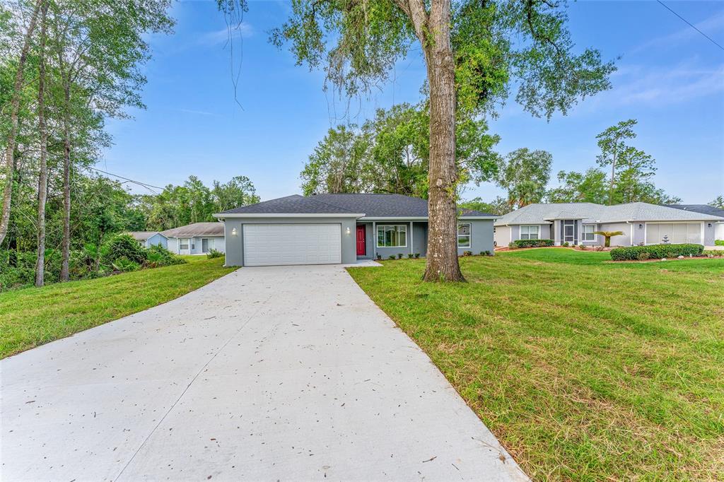 A single-story house with a gray exterior, a white garage door, and a red front door — 13119 NE 7TH LOOP, SILVER SPRINGS, FL