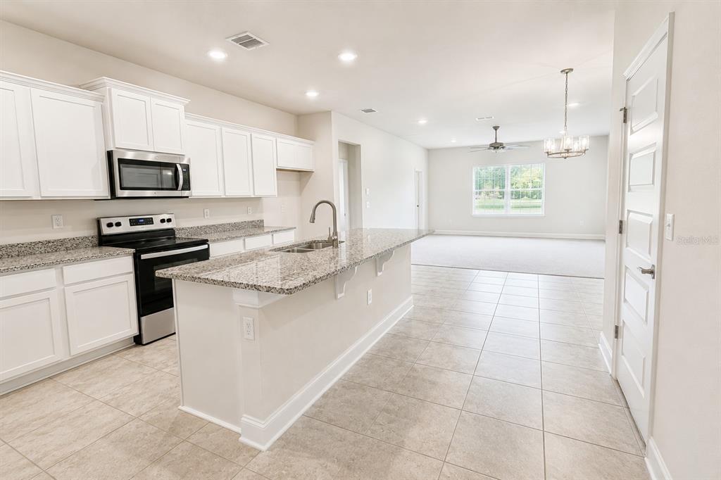 A kitchen with white cabinets, granite countertops, and an island opens to a living area — 3645 BRIARLYNNE WAY, ST CLOUD, FL