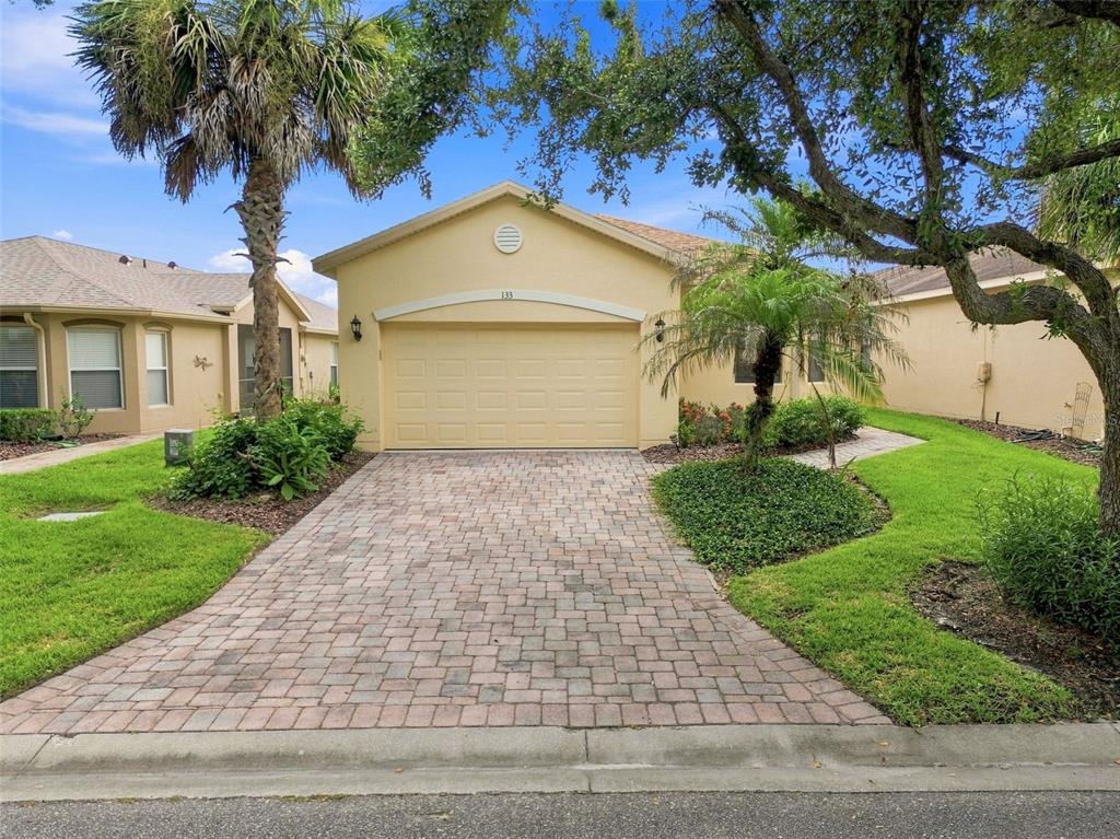A single-story house with a beige exterior, a two-car garage, and a brick paver driveway — 133 GRAND CANAL DRIVE, POINCIANA, FL