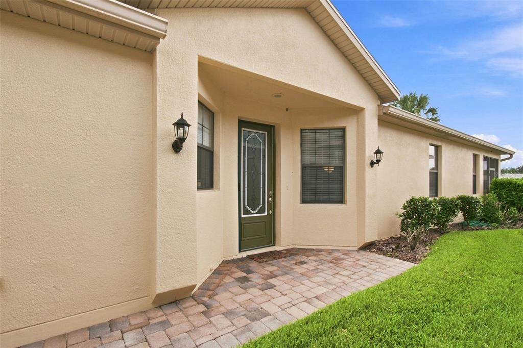 The exterior of a house features a paved entryway, a dark green door, and stucco walls — 133 GRAND CANAL DRIVE, POINCIANA, FL