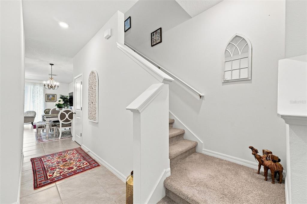 An entryway with a carpeted staircase, tile flooring, and a view into a dining area — 32898 PEZ LANDING LANE, WESLEY CHAPEL, FL