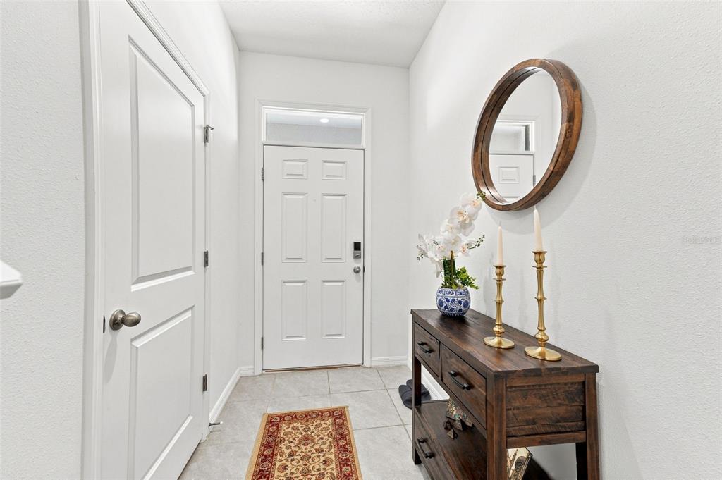 A bright entryway features a white door, a wooden console table, and a round wall mirror — 32898 PEZ LANDING LANE, WESLEY CHAPEL, FL