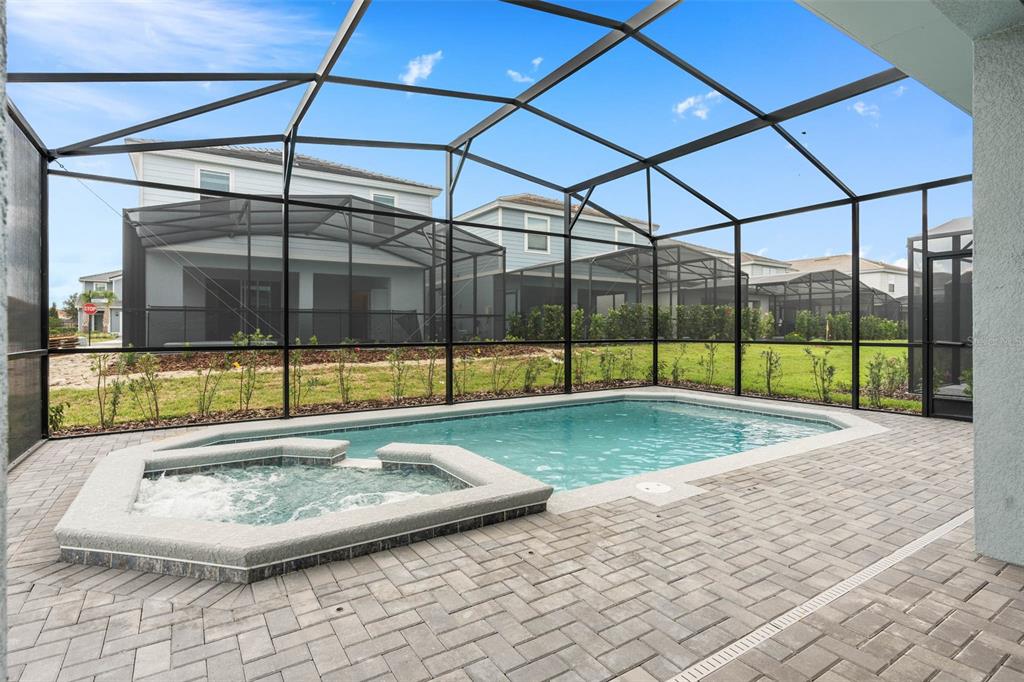 A screened-in patio features a swimming pool, a raised hot tub, and paver flooring — 7180 OAKMOSS LOOP, DAVENPORT, FL
