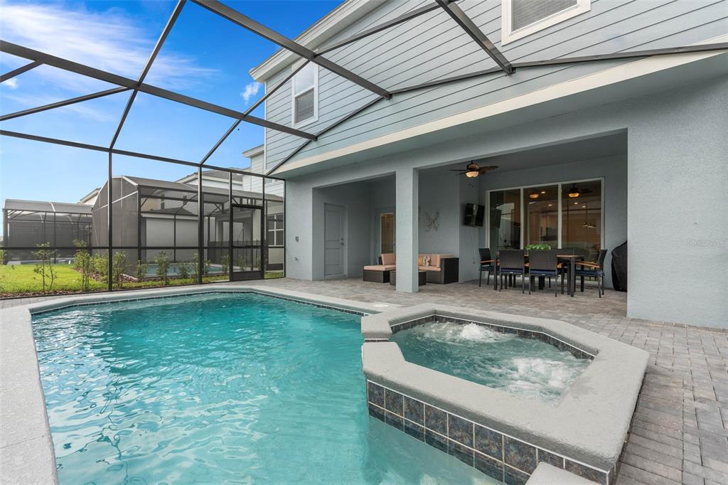 A screened-in patio features a swimming pool, a raised hot tub, and outdoor dining furniture — 7180 OAKMOSS LOOP, DAVENPORT, FL