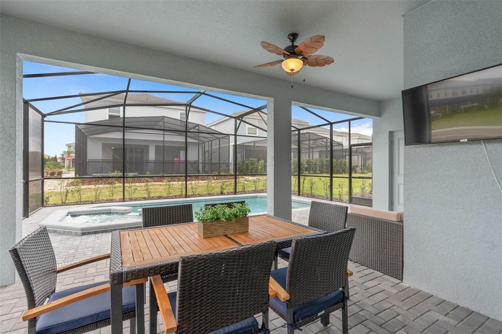A covered patio features a dining set, a ceiling fan, and a screened-in swimming pool — 7180 OAKMOSS LOOP, DAVENPORT, FL