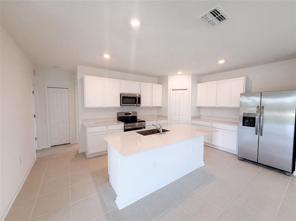A kitchen features white cabinets, stainless steel appliances, a central island, and light tile flooring — 4373 RIVER BEACON BOULEVARD, DAVENPORT, FL