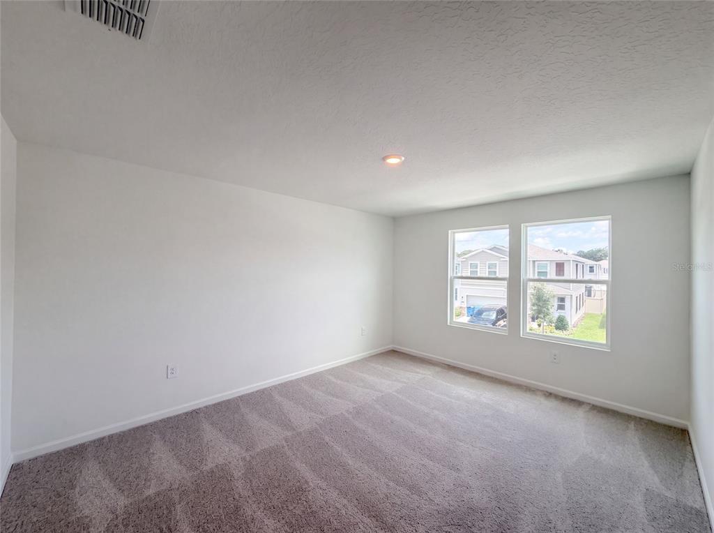 An empty bedroom features white walls, gray carpeting, and two windows overlooking a suburban street — 4373 RIVER BEACON BOULEVARD, DAVENPORT, FL