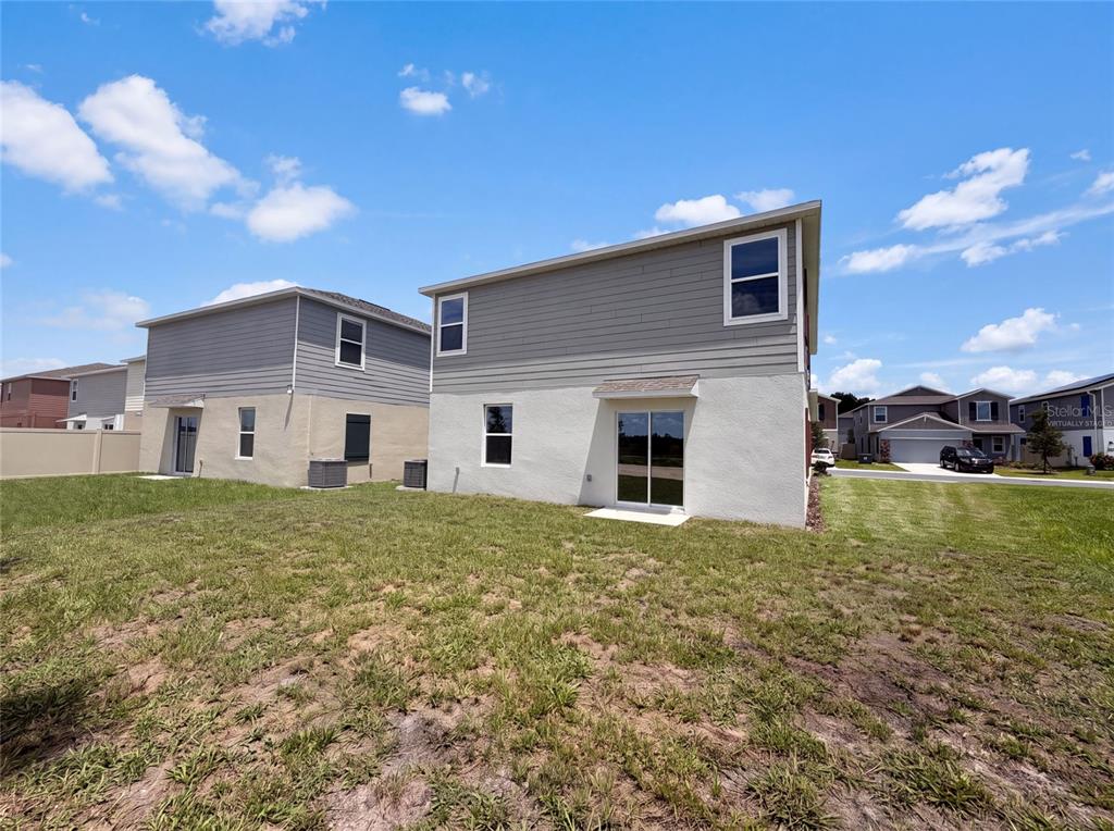 The rear exterior of a two-story house features a sliding glass door and a grassy yard — 4373 RIVER BEACON BOULEVARD, DAVENPORT, FL