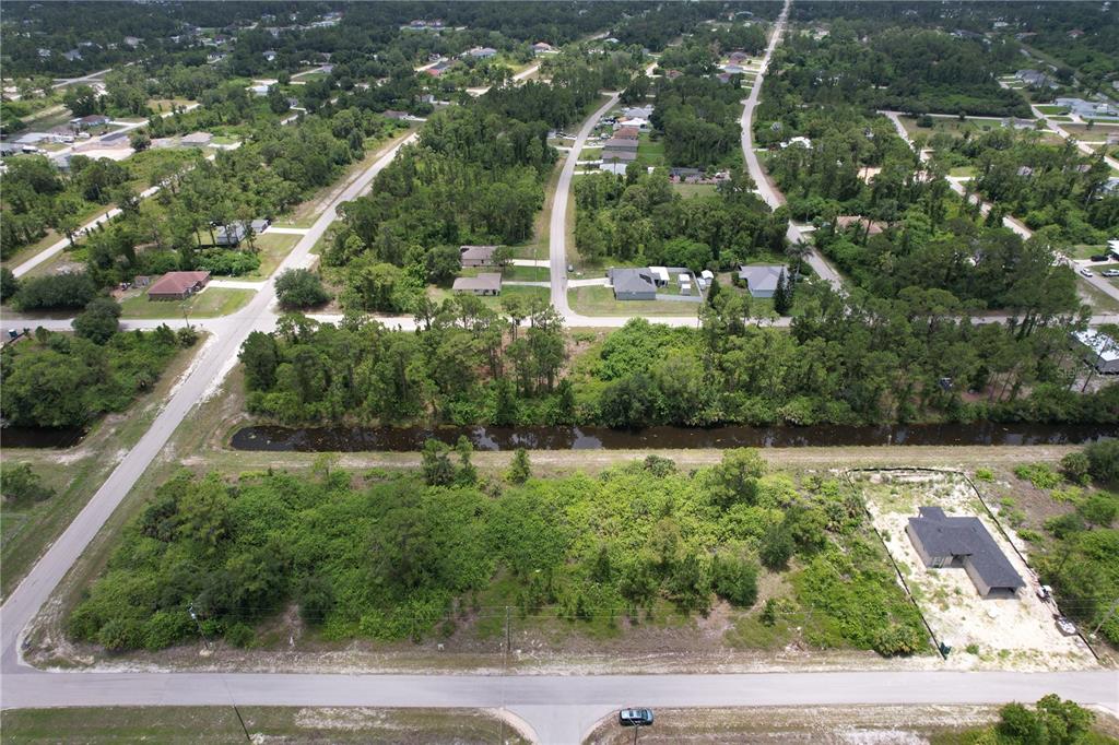 An aerial view shows a vacant lot with a canal, nearby houses, and paved roads — 980 LAKESIDE DRIVE, LEHIGH ACRES, FL
