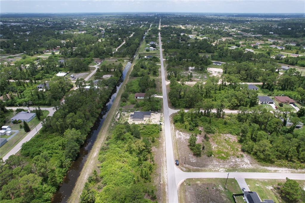 An aerial view shows a paved road running through a wooded residential area with canals — 980 LAKESIDE DRIVE, LEHIGH ACRES, FL