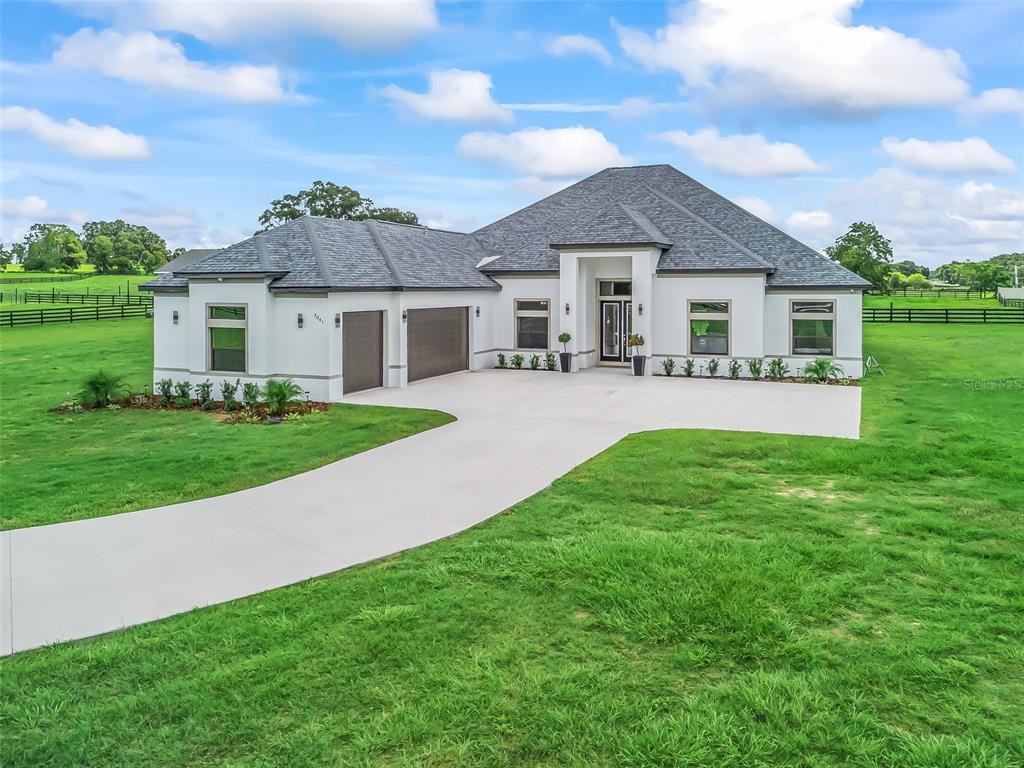 A modern single-story house with a gray roof and white exterior sits on a grassy lot — 7041 NE 22ND COURT ROAD, OCALA, FL
