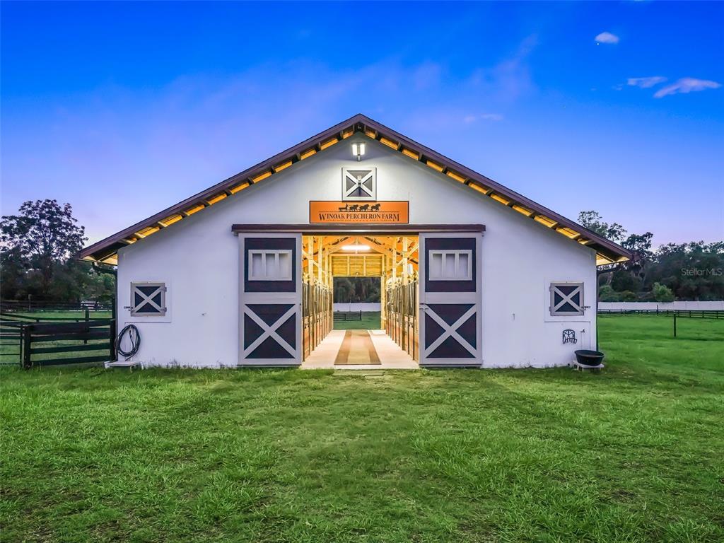 A white barn with a central aisle and sliding doors stands on a grassy field — 7041 NE 22ND COURT ROAD, OCALA, FL