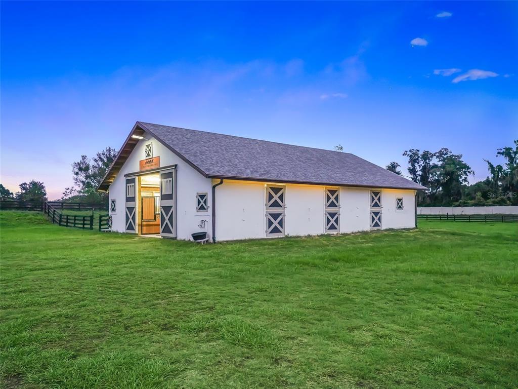 A white barn with a shingled roof stands in a grassy field at dusk — 7041 NE 22ND COURT ROAD, OCALA, FL