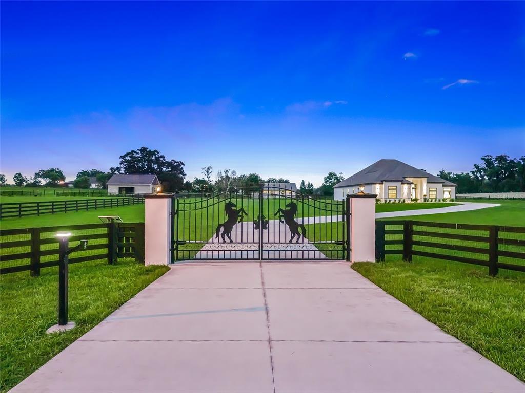 A concrete driveway leads to a gated entrance with horse silhouettes in front of a house — 7041 NE 22ND COURT ROAD, OCALA, FL