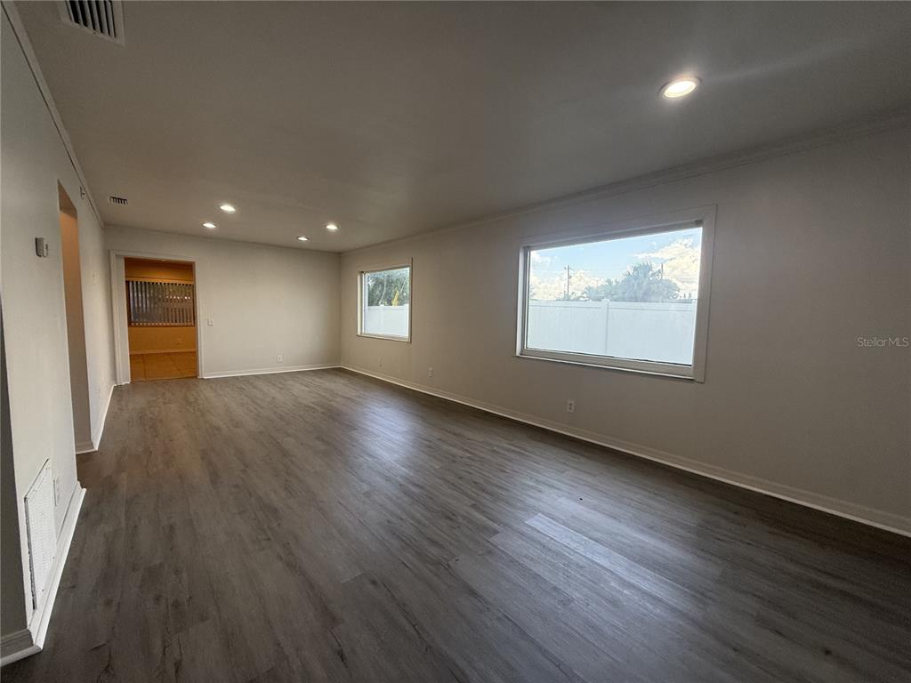 An empty living room features gray wood-look flooring, recessed lighting, and two windows — 5171 98TH AVENUE N, PINELLAS PARK, FL