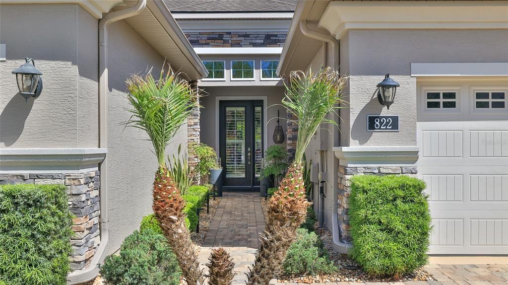 A stone-paved walkway leads to the front entrance of a house with stucco walls — 822 ALDENHAM LANE, ORMOND BEACH, FL