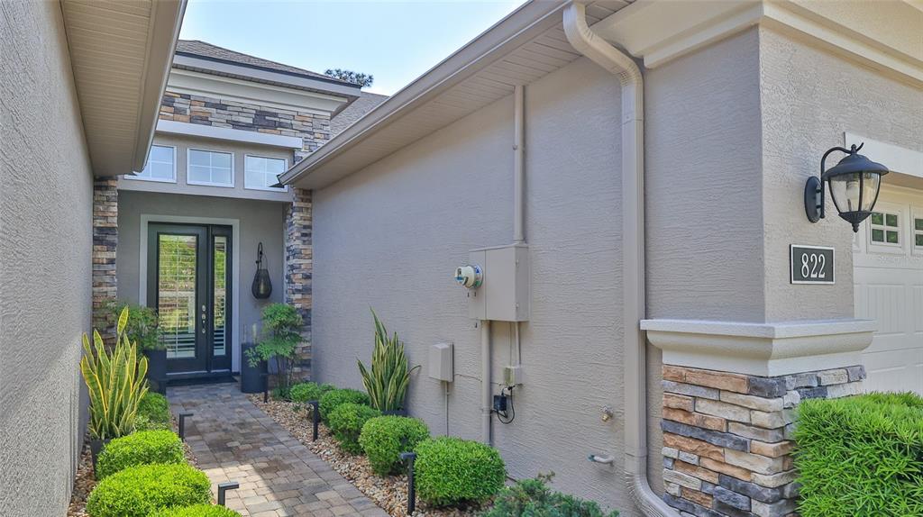 A stone-accented house exterior features a paved walkway leading to a glass-paneled front door — 822 ALDENHAM LANE, ORMOND BEACH, FL