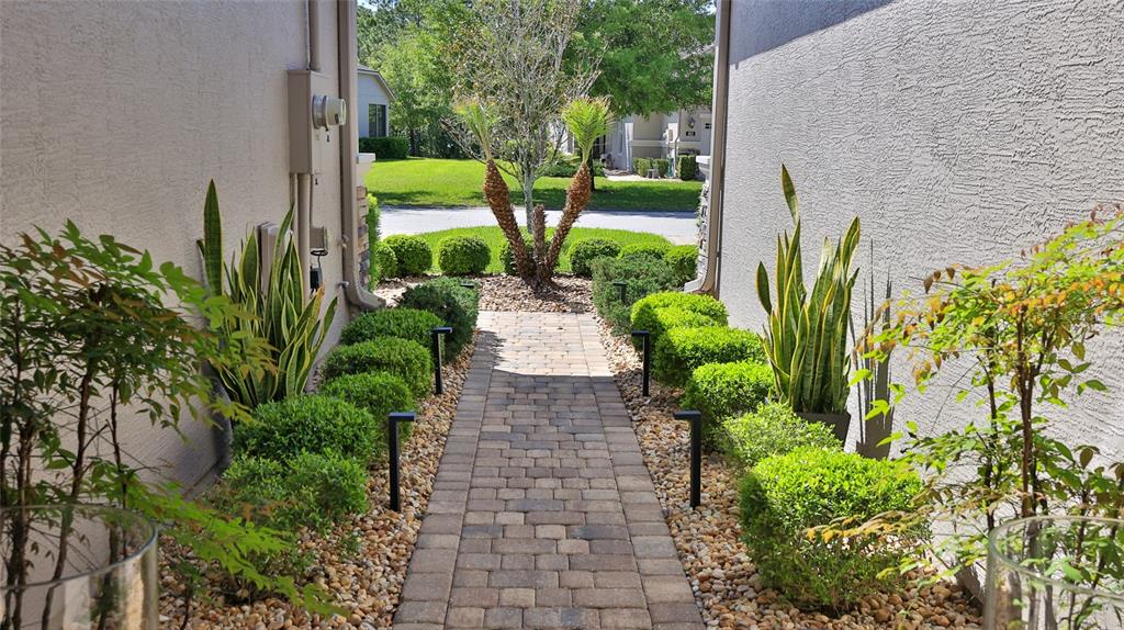 A paved walkway leads between two stucco walls lined with shrubs and snake plants — 822 ALDENHAM LANE, ORMOND BEACH, FL