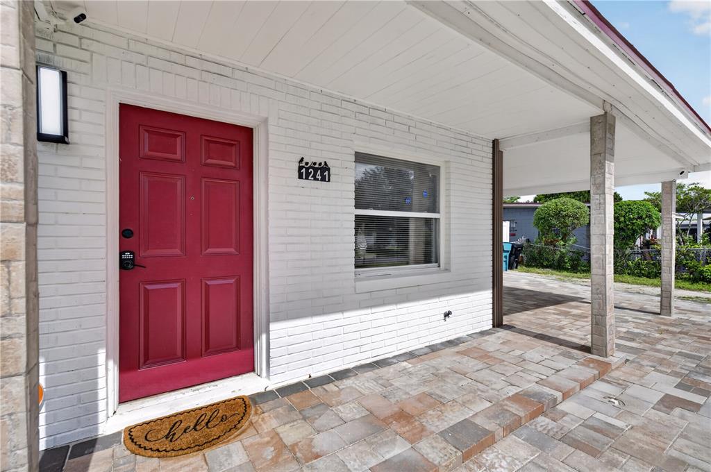 A red front door sits beside a window on a white brick house with pavers — 1241 DEEROCK DRIVE, ORLANDO, FL