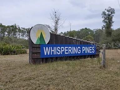 A wooden sign with the text Whispering Pines stands in a grassy, wooded field — 224 PLUMOSA DRIVE, GEORGETOWN, FL