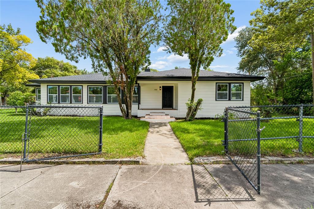 A single-story white house with a dark roof sits behind a chain-link fence — 400 PLUMOSA DRIVE, SANFORD, FL