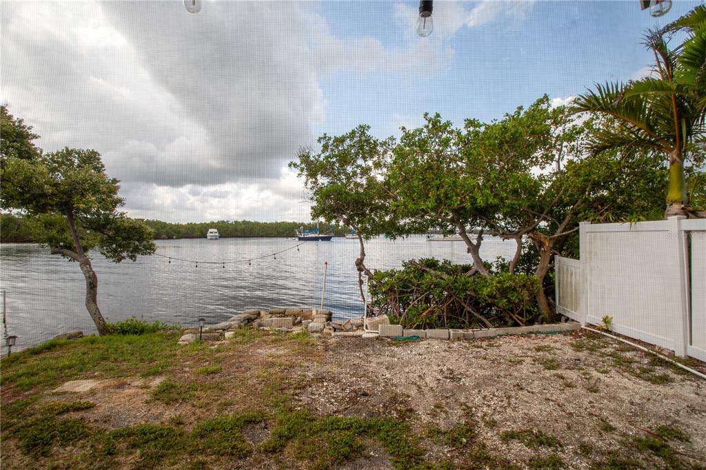 A view of a waterfront backyard with trees, a white fence, and boats offshore — 3312 W SHELL POINT ROAD, RUSKIN, FL