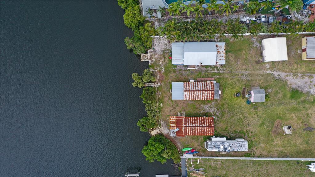 An aerial view shows three small houses with metal roofs situated along a waterfront — 3312 W SHELL POINT ROAD, RUSKIN, FL