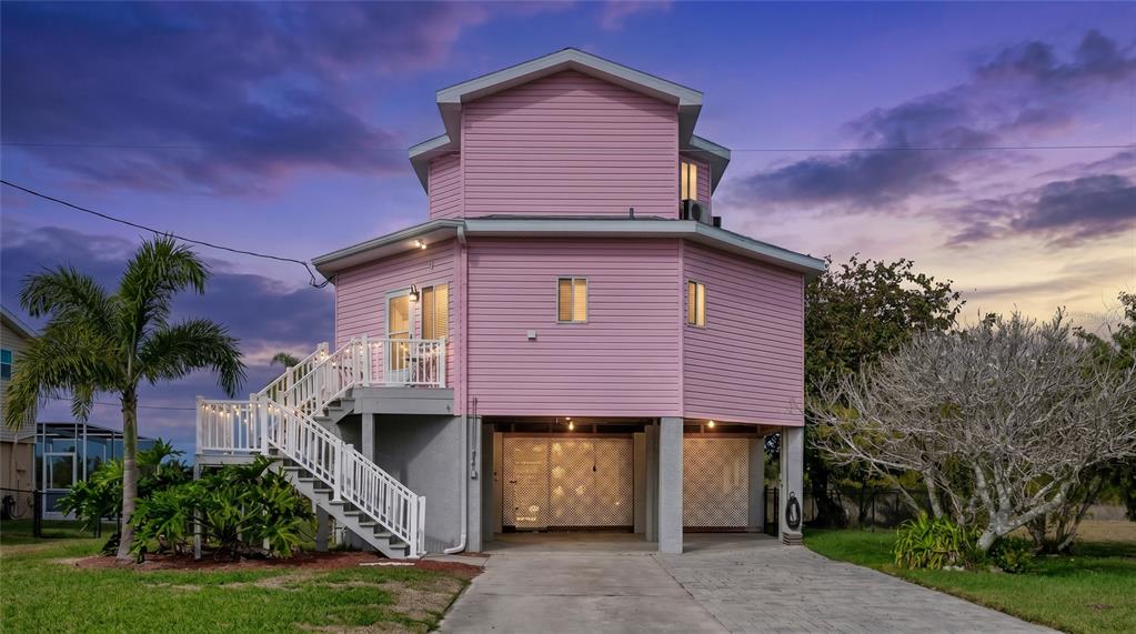 A pink, elevated stilt house with a white staircase and a concrete driveway at dusk — 3460 CRAPE MYRTLE DRIVE, HERNANDO BEACH, FL