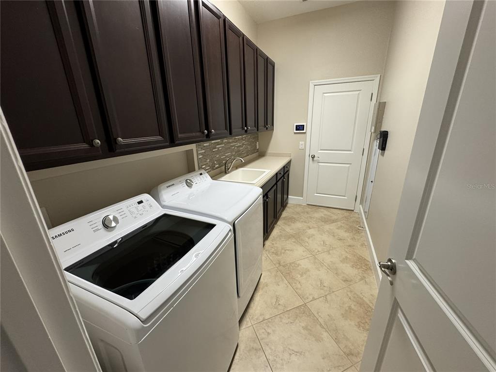 A laundry room features dark wood cabinets, white appliances, a sink, and tile flooring — 5847 PALMER RANCH PARKWAY, SARASOTA, FL