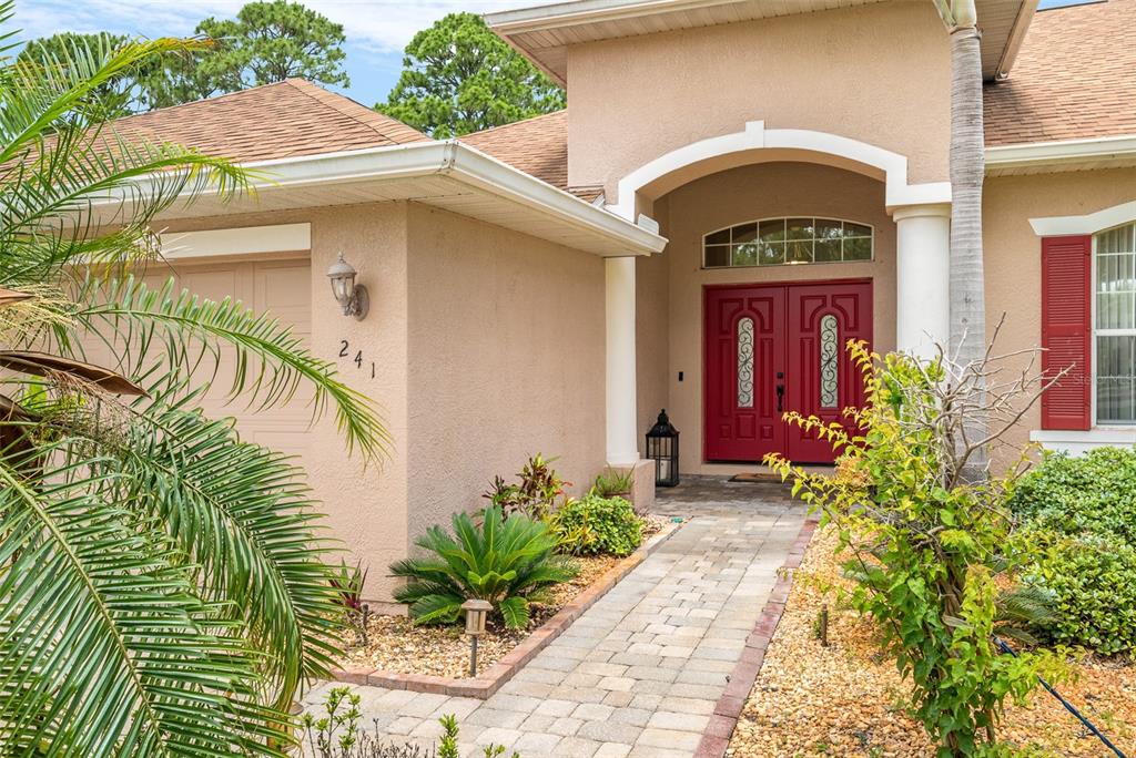 The exterior of a beige house features a red double front door and a walkway — 241 DEVLIN COURT, PALM BAY, FL