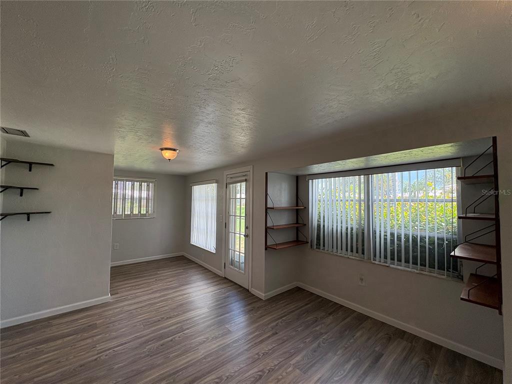 A room with wood-look flooring, multiple windows with vertical blinds, and built-in wall shelving — 3276 BRUNSWICK LANE UNIT 705, SARASOTA, FL