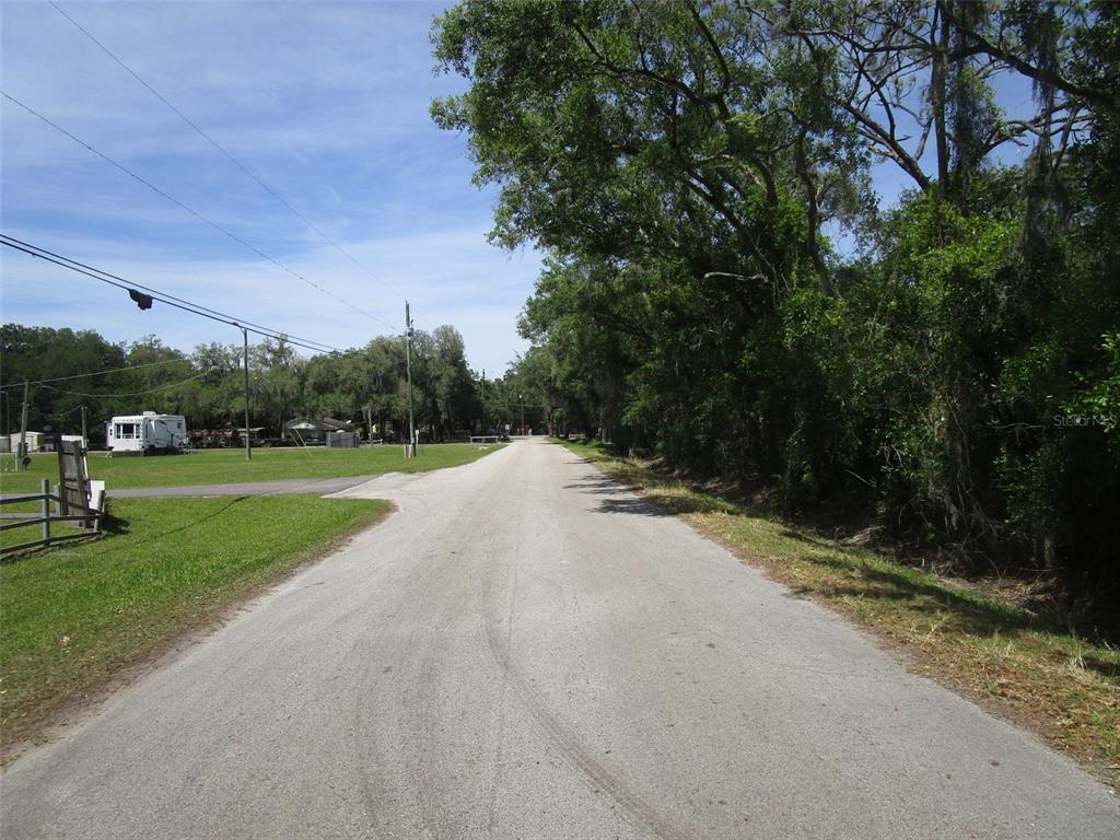 A paved road stretches forward between a grassy lot with a trailer and dense trees — 00 CASTLEWOOD ROAD, SEFFNER, FL