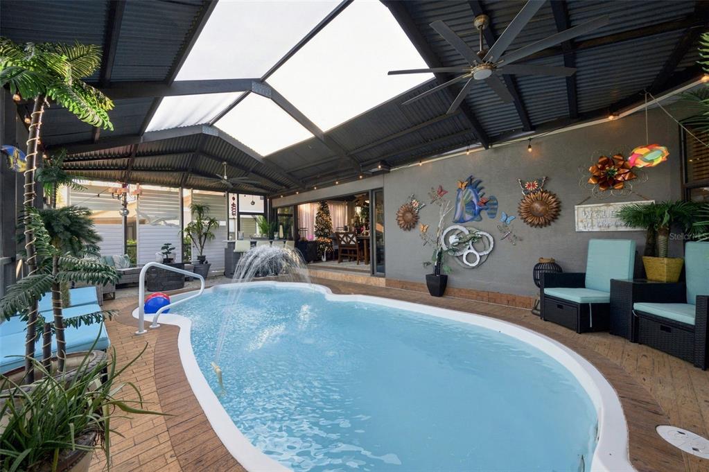 A covered patio features a swimming pool with a fountain, outdoor seating, and wall decorations — 8136 GOLF CLUB COURT, HUDSON, FL