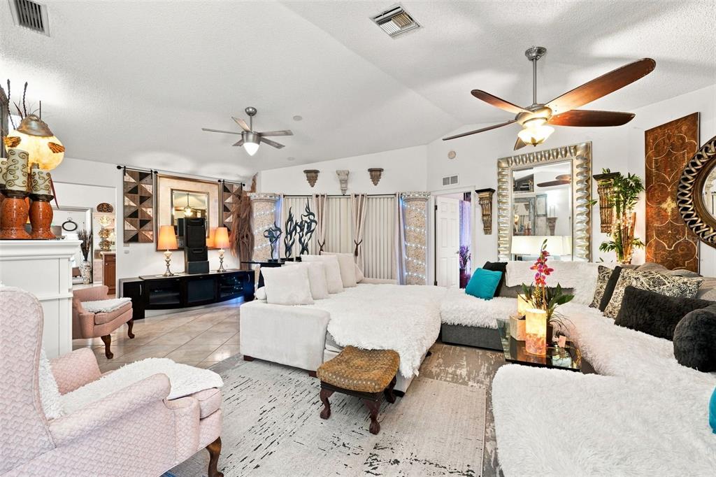 A spacious living room features a large white sectional sofa, vaulted ceilings, and multiple mirrors — 8136 GOLF CLUB COURT, HUDSON, FL
