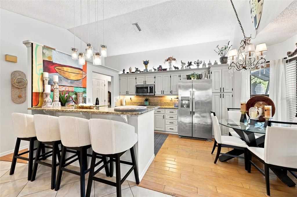 A kitchen features white cabinets, stainless steel appliances, a granite island, and a dining area — 8136 GOLF CLUB COURT, HUDSON, FL