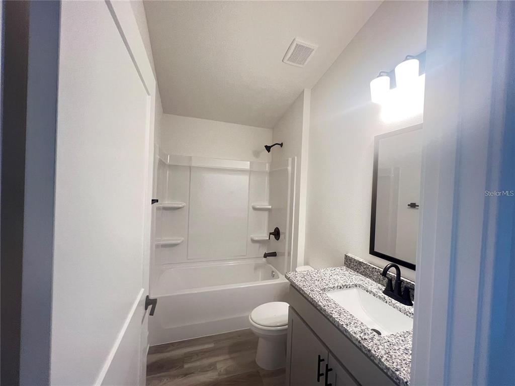 A bathroom features a white tub-shower combo, a gray vanity with granite countertop, and flooring — 3635 LINDBERGH STREET, LAKELAND, FL