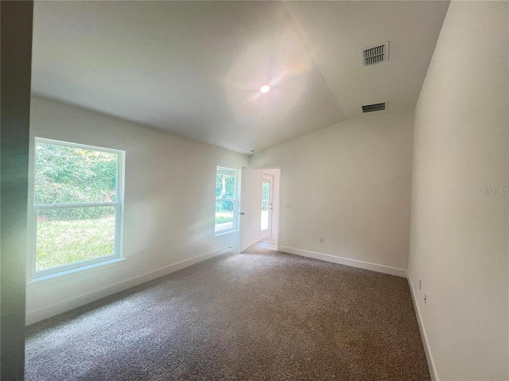 An empty bedroom with beige carpet, white walls, a vaulted ceiling, and two windows — 3635 LINDBERGH STREET, LAKELAND, FL